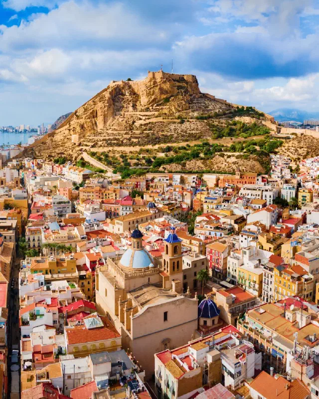 Kleurrijke foto van de stad met daarbovenuitreikend het kasteel de Santa Barbara in Alicante.