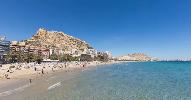 Brede foto van zonnig Playa del Postiguet met op de achtergrond de Monte Benacantil met Castillo de Santa Barbara. Brede foto van zonnig Playa del Postiguet met op de achtergrond de Monte Benacantil met Castillo de Santa Barbara.