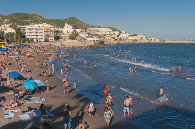 Het populaire strand Platja de Sant Sebastia in Sitges met goudkleurig zand en de kerk op de achtergrond